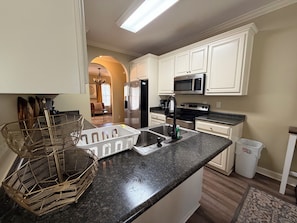 A kitchen with white cabinets, a stainless steel refrigerator, a microwave, a sink, and a dish rack.