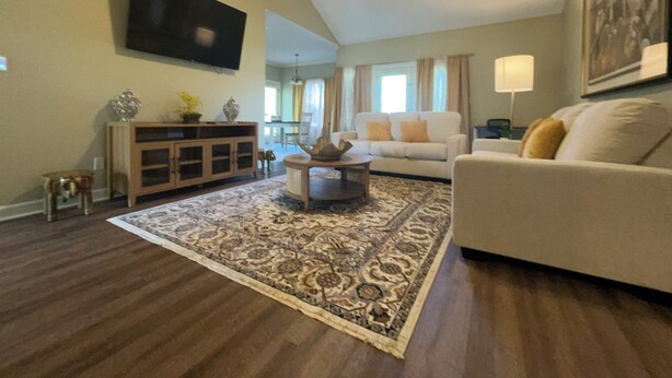 A living room with a large flat-screen TV mounted on the wall, a ceiling fan, a sofa, a coffee table, and a patterned rug. - Lovely 3 bedroom, 2 Bath Home in Lake Park near I-75! (Lake Park)