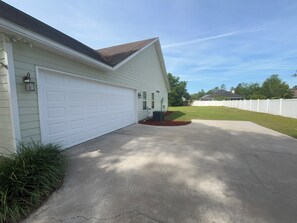 A single-story house with a white garage door, a concrete driveway, and a small front yard with a lawn and a white fence. - Lake Park 3BR • 9 Beds • Near I-75 • Groups (Lake Park)