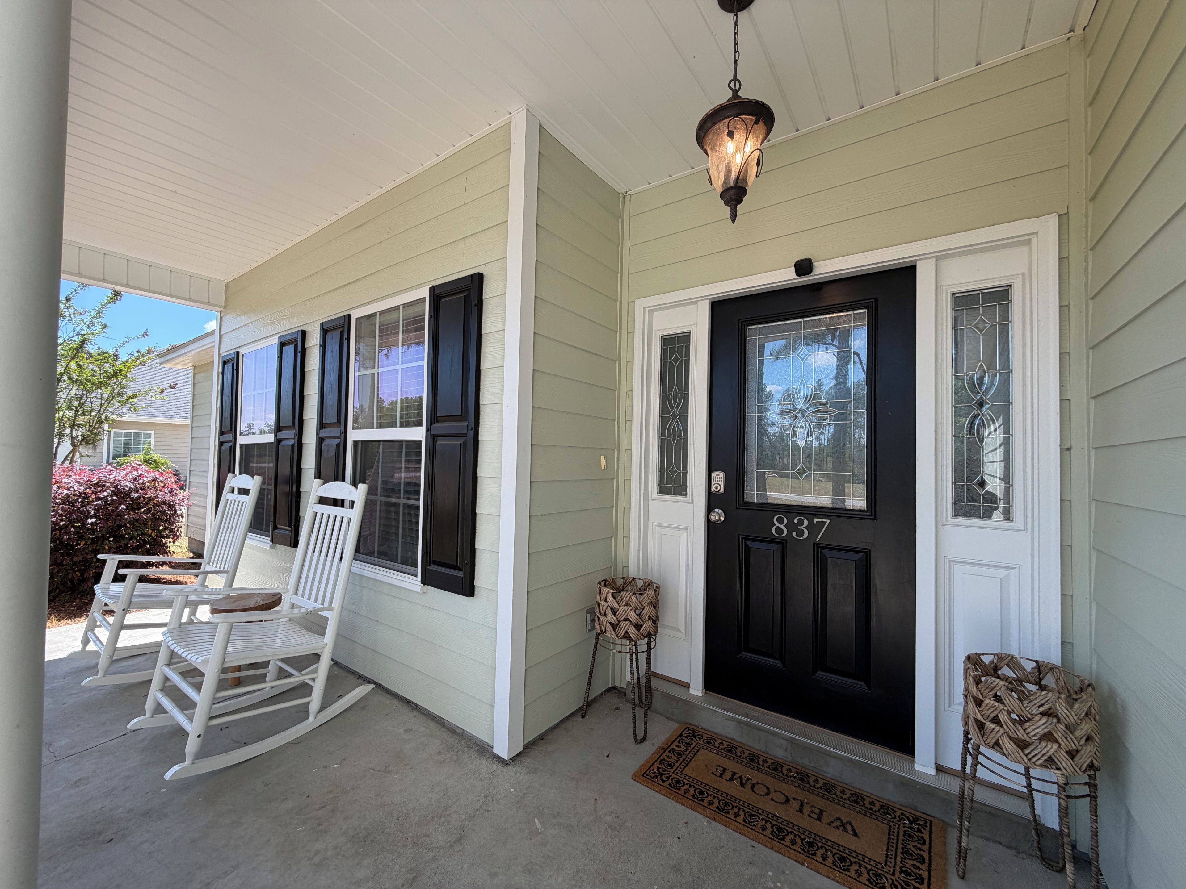 A house with a black front door, white rocking chairs, and a porch.