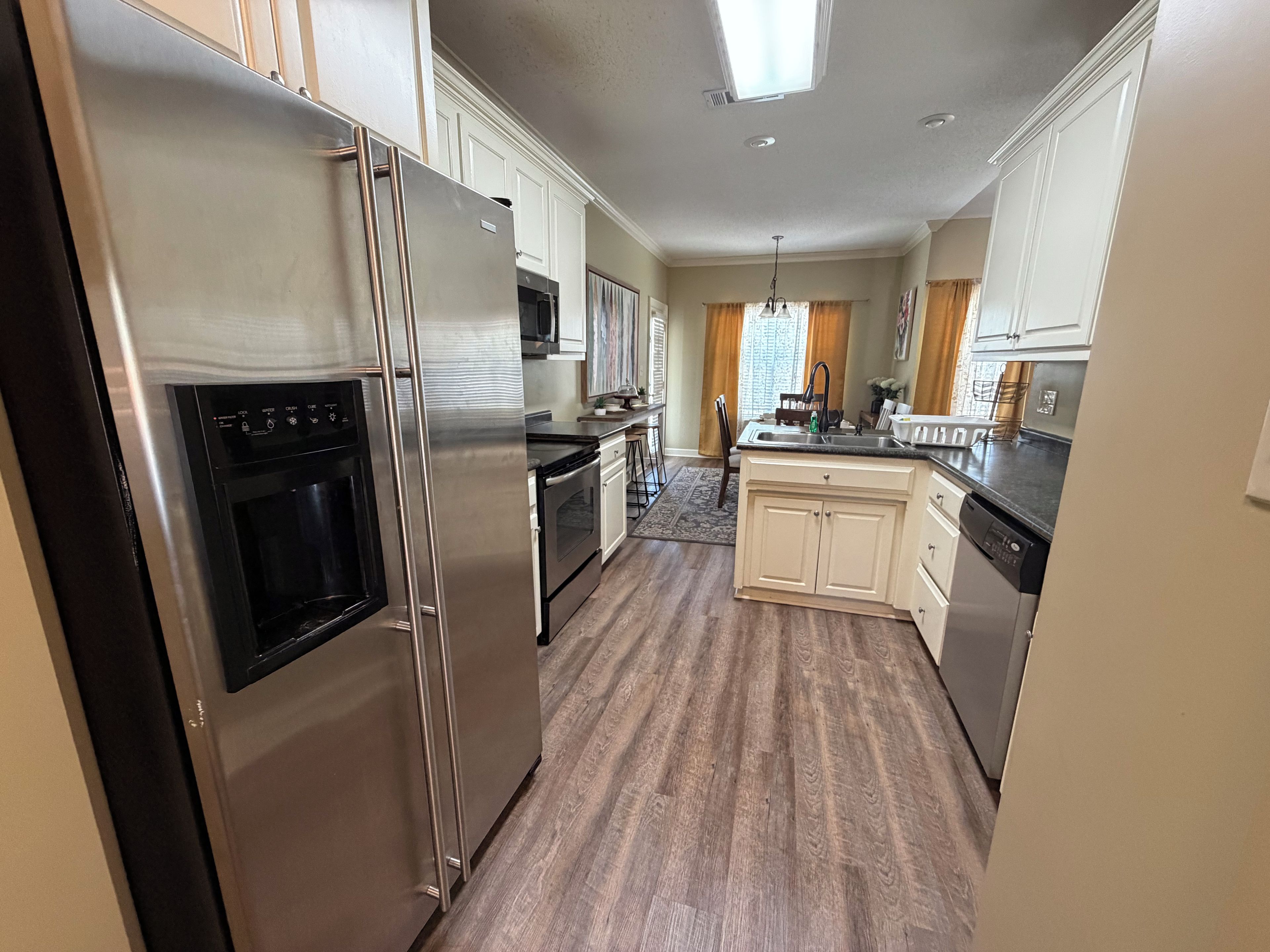 A kitchen with stainless steel appliances, wooden flooring, and white cabinetry.