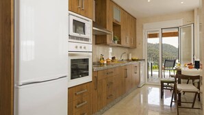 A kitchen with wooden cabinets, a white refrigerator, a built-in oven, and a dining area with a table and chairs. - Villa Fuente by Villa Plus (Frigiliana)