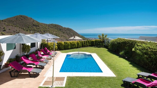 A pool area with lounge chairs and umbrellas, surrounded by greenery and a view of the sea. - Villa Fuente by Villa Plus (Frigiliana)
