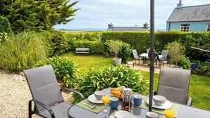 Een ontbijttafel met stoelen, een bankje en uitzicht op de zee en huizen op de achtergrond.