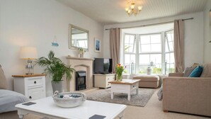 Een woonkamer met een open haard, televisie, bank en een eettafel met een schaal en kaarsen.
