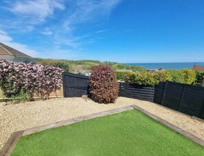 Un jardin avec une pelouse artificielle, une clôture en bois et une vue sur la mer.