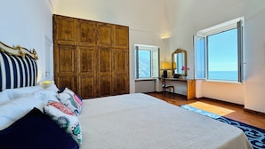 A bedroom with a large bed, a wooden wardrobe, a desk with a laptop, a chair, and a view of the sea through large windows. - YourHome - La Casa di Chiara (Positano)