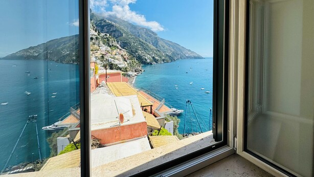 A coastal view from a window overlooking a marina with boats, a hillside village, and a mountain in the background. - YourHome - La Casa di Chiara (Positano)