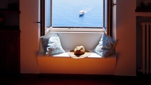 A room with a window overlooking the sea, a small bench with a hat, and a radiator. - YourHome - La Casa di Chiara (Positano)