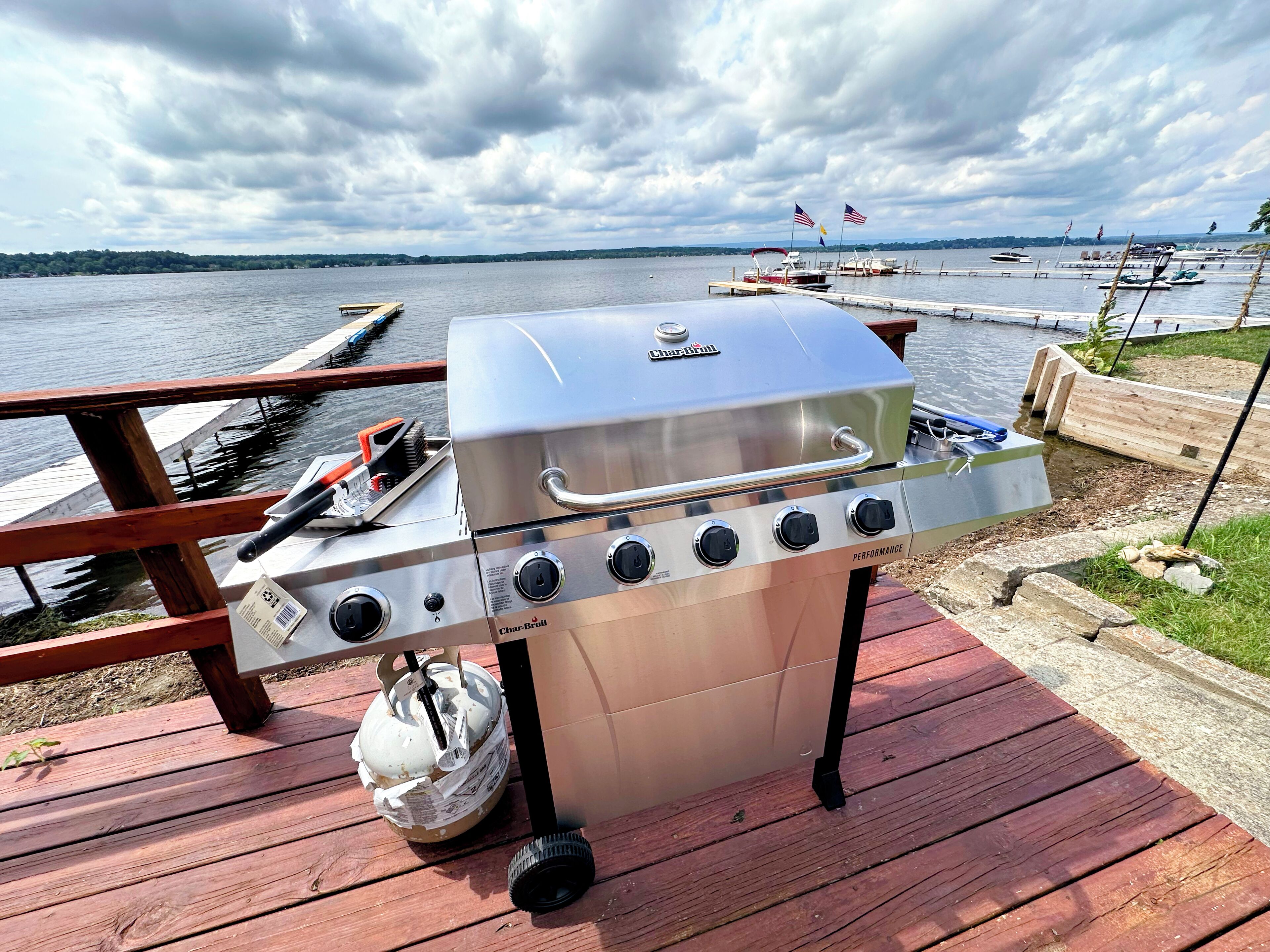 A Char-Broil grill with four burners on a wooden deck by a lake.