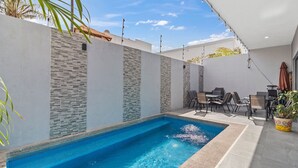 A swimming pool with tiled edges, surrounded by a white wall with stone accents, and a patio area with chairs and a table. - Casa Bella Puerto Vallarta (Puerto Vallarta)