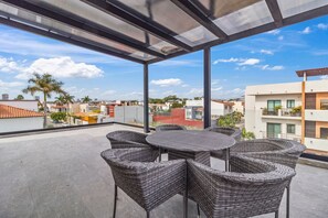 A covered outdoor seating area with wicker furniture, a clear view of the surrounding buildings, and a blue sky with clouds. - Casa Bella Puerto Vallarta (Puerto Vallarta)