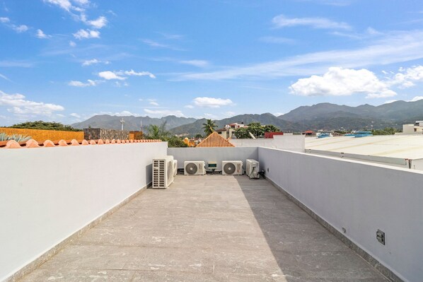 A rooftop terrace with air conditioning units, a view of mountains, and a clear sky.
