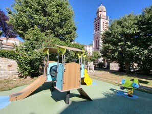 Explore the vintage-style playground with a slide and climbing section, surrounded by lush greenery and a historic clock tower.