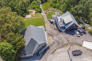 An aerial view of a property with two large buildings, a driveway, and surrounding greenery.