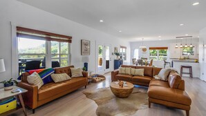 A spacious living room with two brown leather sofas, a wooden coffee table, and a large window with a view of greenery. - Charming Lakeside Escape w/ Large Deck & Firepit! (Clarkson)