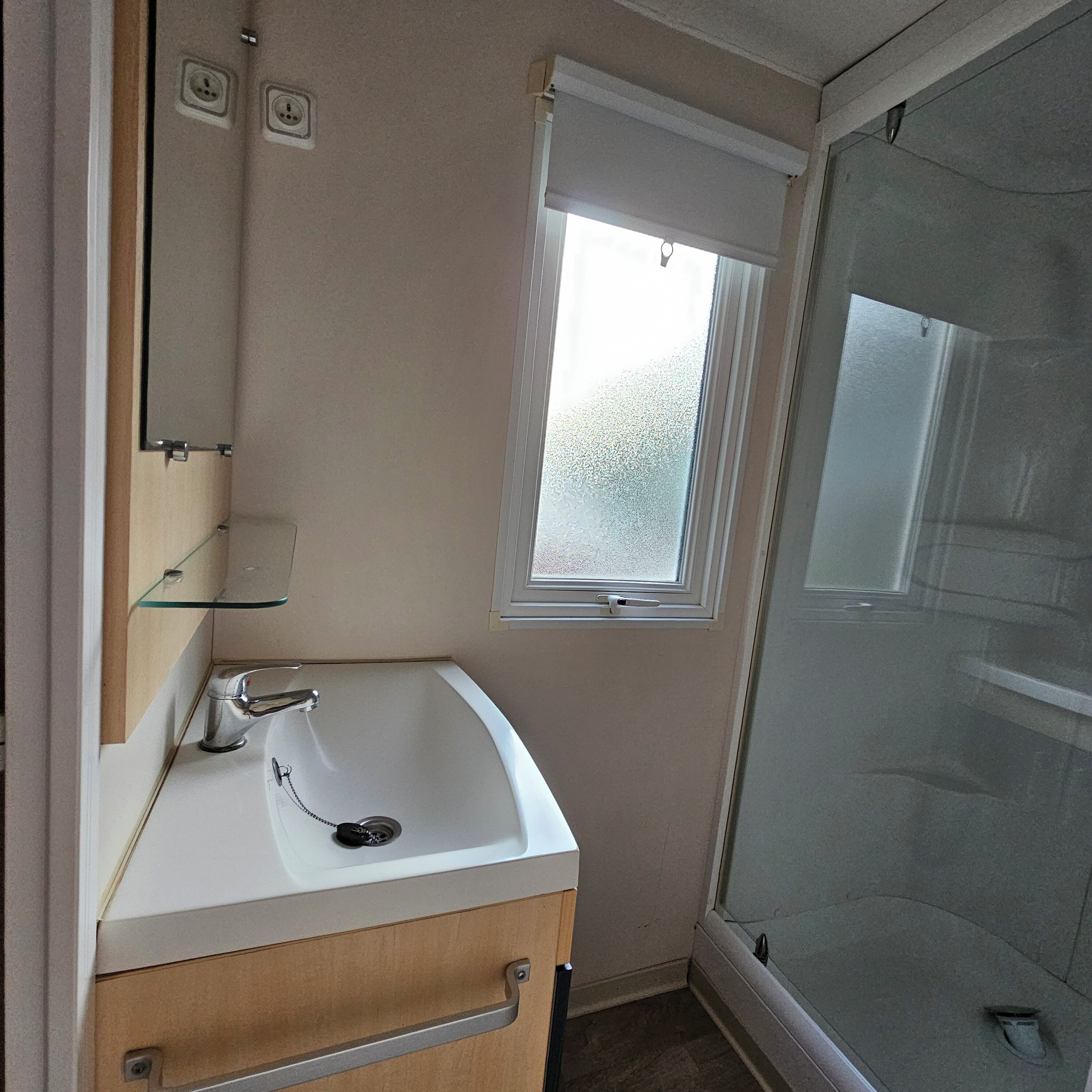A bathroom with a white sink, a mirror, a window, and a shower area.