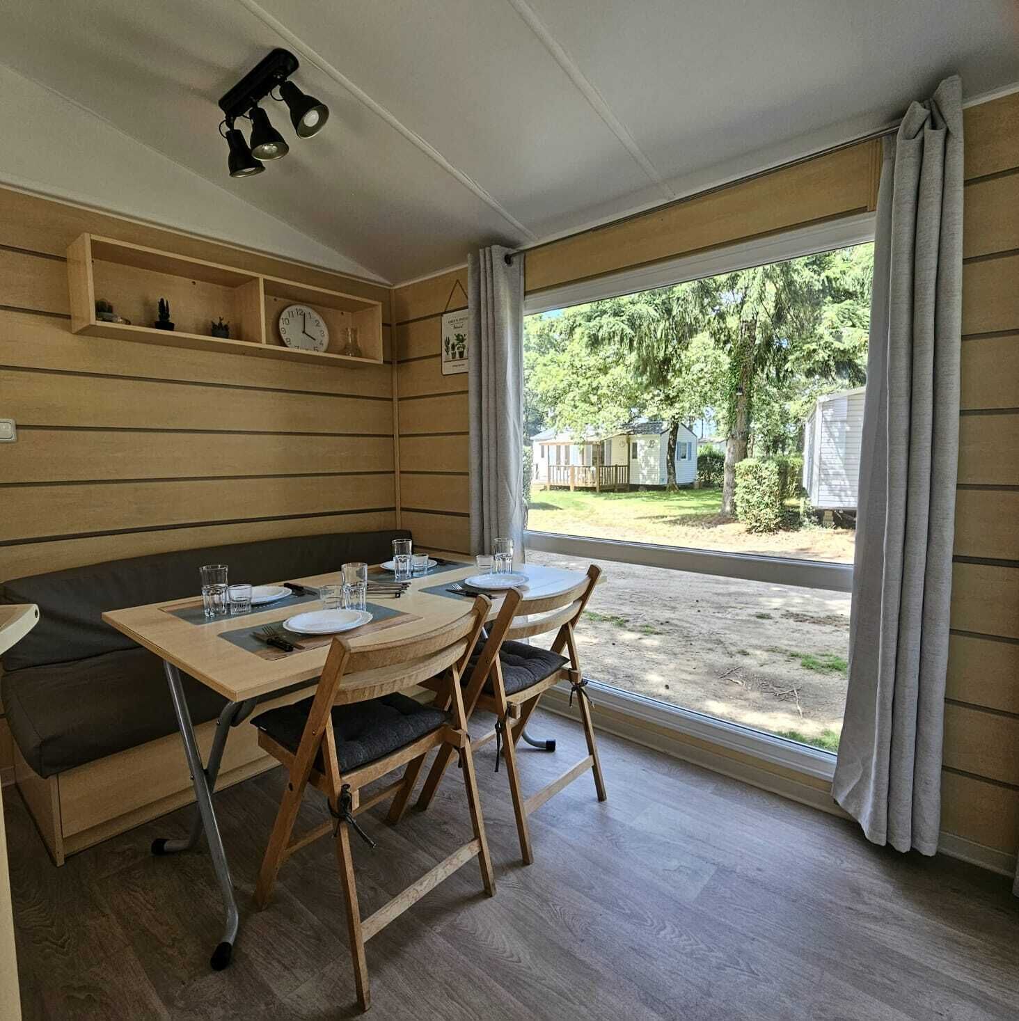 Un comedor con una mesa de madera, sillas y un banco. Hay estantes con adornos y un reloj en la pared.