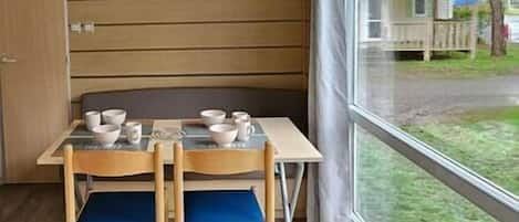 Un'angolare sala da pranzo con tavolo e sedie, una finestra che si affaccia su una casa e alberi, e un muro in legno.