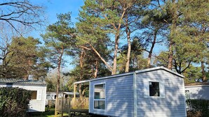 Une maison mobile dotée d’une véranda et d’une fenêtre, entourée d’arbres et d’herbe.
