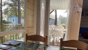 A table with a "Bienvenue" sign, two glasses of fruit, and a view of a deck area with chairs and a house in the background.