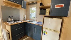 A compact kitchen with a gas stove, kettle, coffee maker, microwave, and a refrigerator.