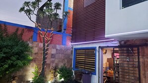 A modern building with a mix of brick and wooden facades, a visible sign, and a small garden area with plants and a tree.