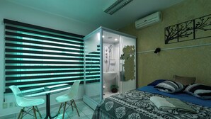 A modern bedroom with a glass shower enclosure, a bed with patterned bedding, a white table with chairs, and a wall-mounted air conditioner.