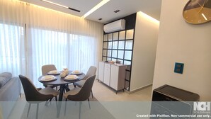 A modern dining area with a round table set for four, a sofa, and a kitchen area with a window and an air conditioning unit.