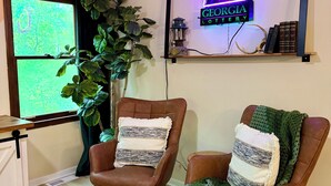 A cozy room with two leather armchairs, a large potted plant, a neon sign, and a rustic wooden shelf. - Perfectly Pink & Cozy 2-bedroom cabin in charming Waverly Hall (Waverly Hall)