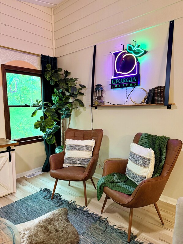 A cozy room with two leather armchairs, a large potted plant, a neon sign, and a rustic wooden shelf. - Perfectly Pink & Cozy 2-bedroom cabin in charming Waverly Hall (Waverly Hall)
