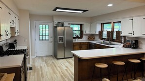 A modern kitchen with white cabinets, a stainless steel refrigerator, a built-in stove, and a large island with bar stools. - Perfectly Pink & Cozy 2-bedroom cabin in charming Waverly Hall (Waverly Hall)