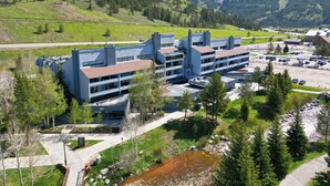A modern hotel with a parking lot, surrounded by mountains and greenery. - Pet Friendly, Spacious, Mountain Views SB102 (Copper Mountain)
