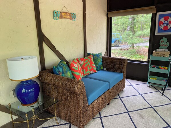 A wicker sofa with colorful cushions, a glass table with a blue vase, and a sign reading "Gone to the beach".