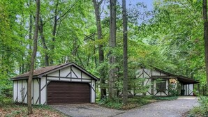 A cabin with a garage and a small porch, surrounded by dense forest. - Charming 3-bedroom cottage with AC in marvelous Saugatuck close to trails (Saugatuck)