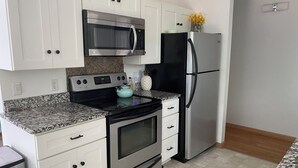 A modern kitchen with white cabinetry, stainless steel appliances, and a granite countertop. - Charming 3-bedroom cottage with AC in marvelous Saugatuck close to trails (Saugatuck)