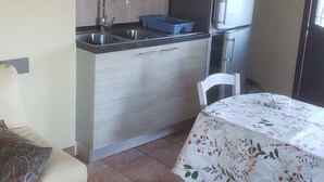 Une cuisine compacte équipée d’un évier, d’une cuisinière et d’un réfrigérateur. Un coin repas avec une table et des chaises est également disponible.