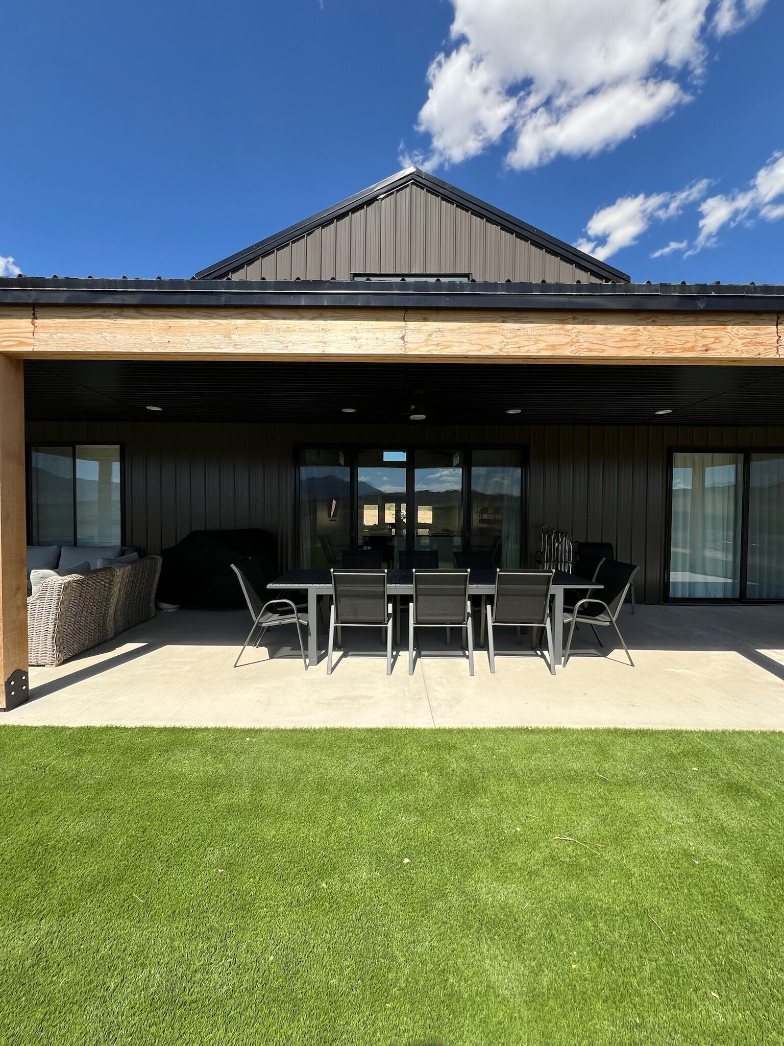 Una casa moderna con patio coperto, zona pranzo con tavolo e sedie e barbecue.