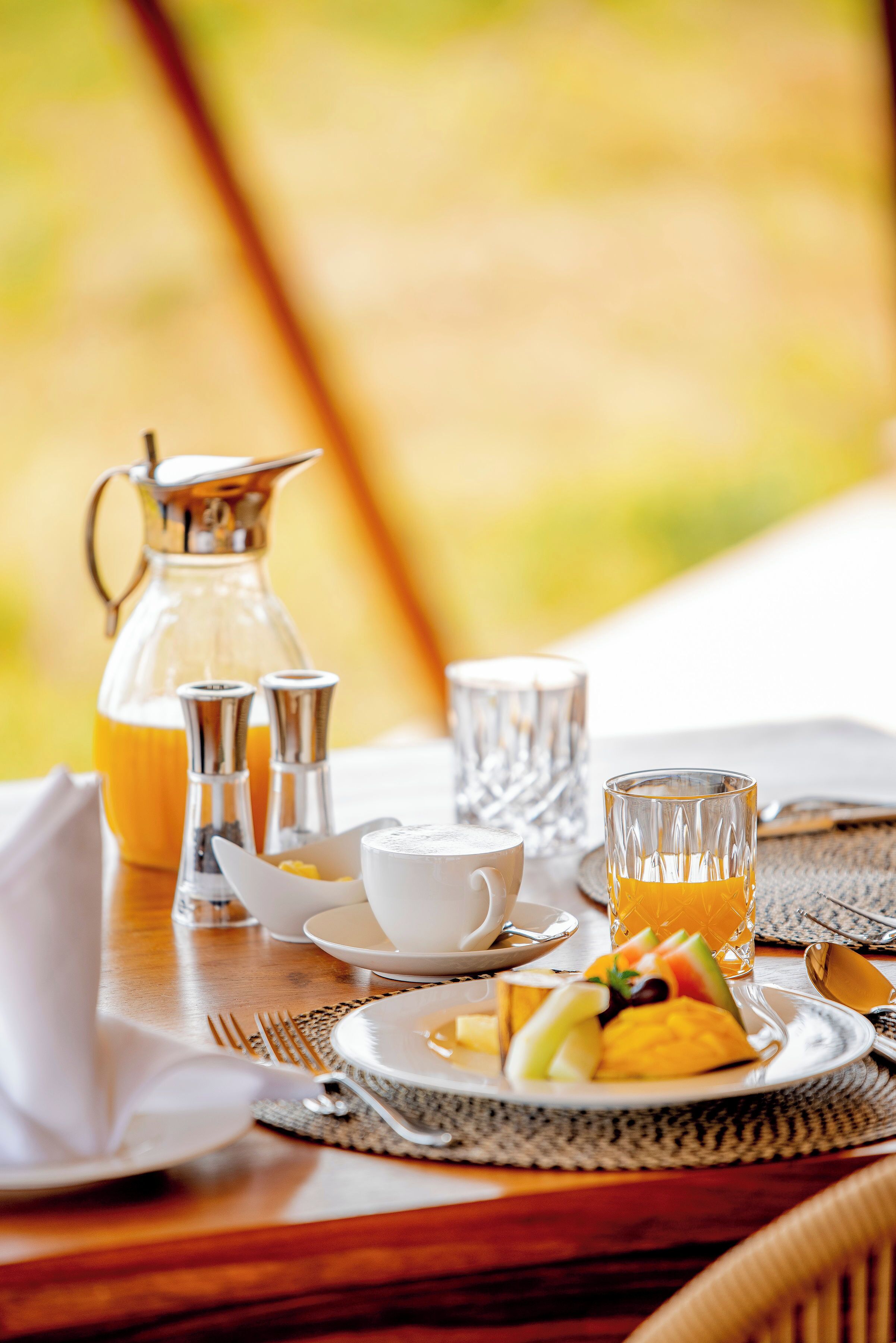 A breakfast table with a pitcher, salt and pepper shakers, a cup, a glass, and a plate with fruit and eggs.