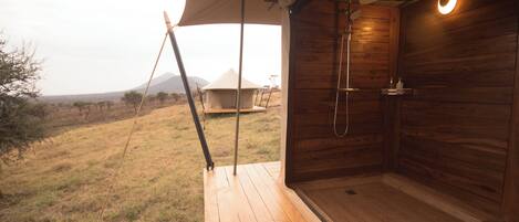 Une terrasse en bois menant à un espace douche avec vue sur une tente et le paysage environnant.