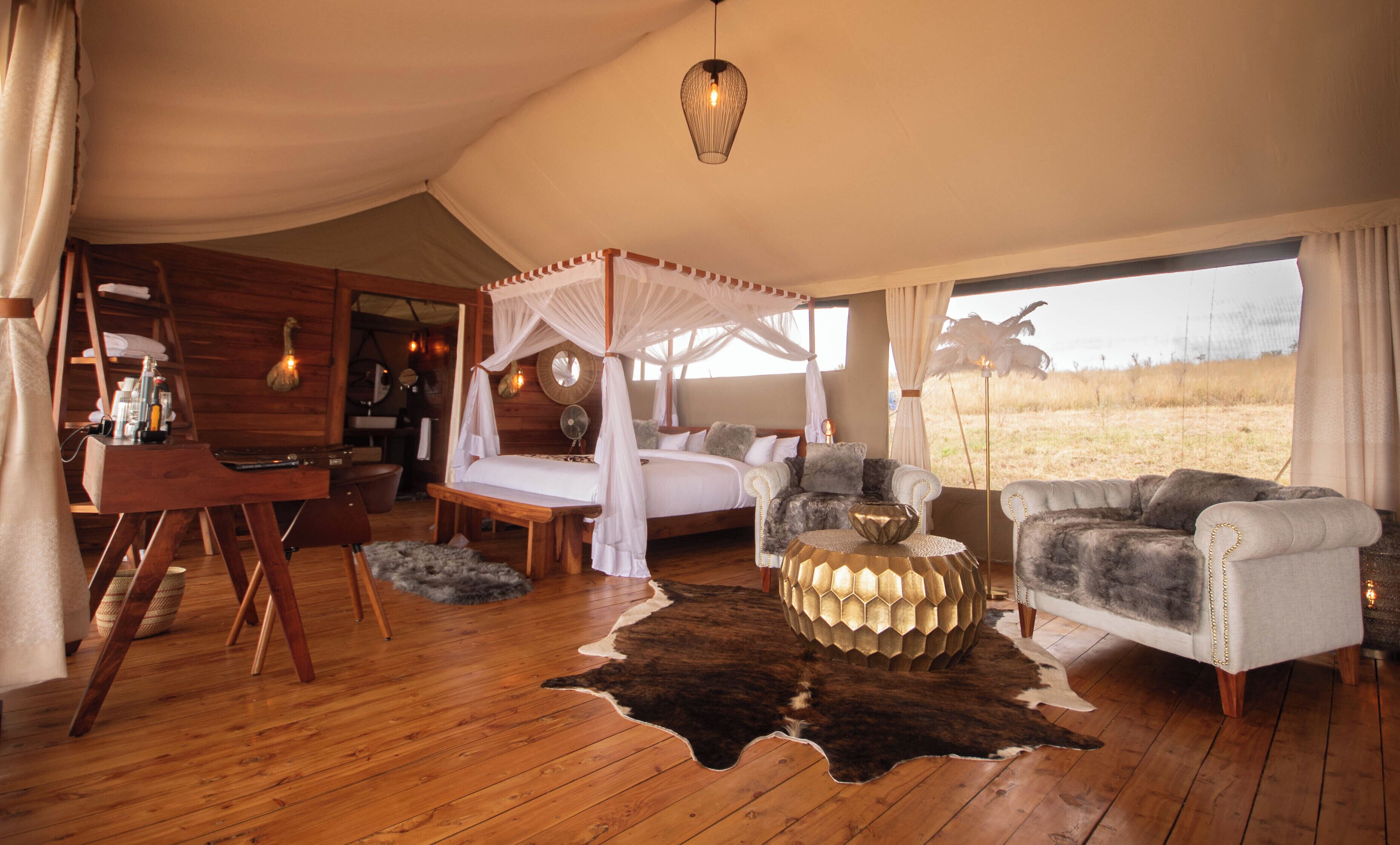 A tented room with a four-poster bed, a sofa, a coffee table, and a view of the outdoors.