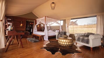 A tented room with a four-poster bed, a sofa, a coffee table, and a view of the outdoors.