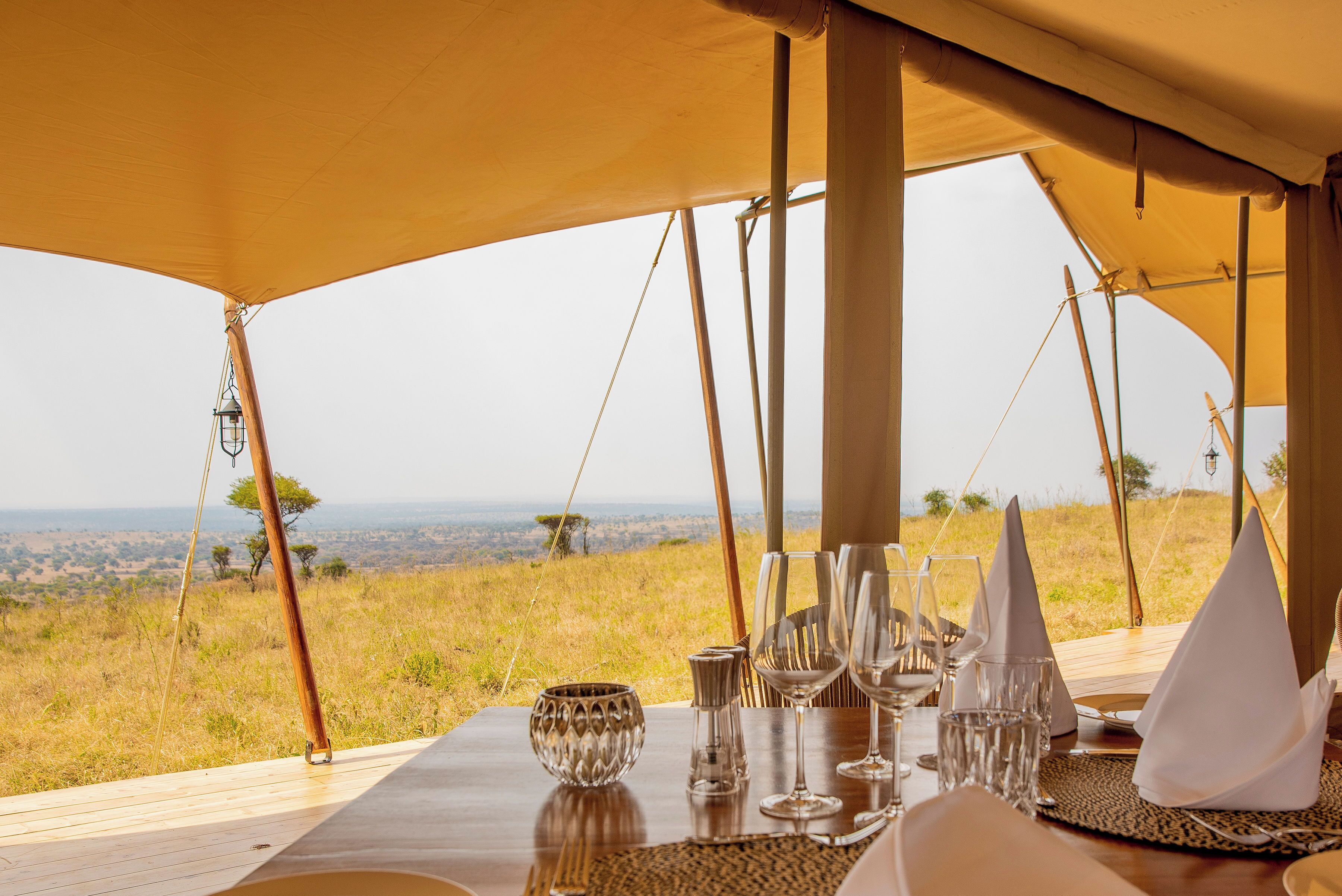 A dining table set for four with a view of a grassy landscape and distant hills.