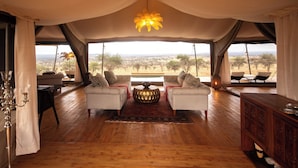 A tented room with two white sofas, a central decorative table, and a view of the savannah. - Serengeti Luxury Retreat (Serengeti)