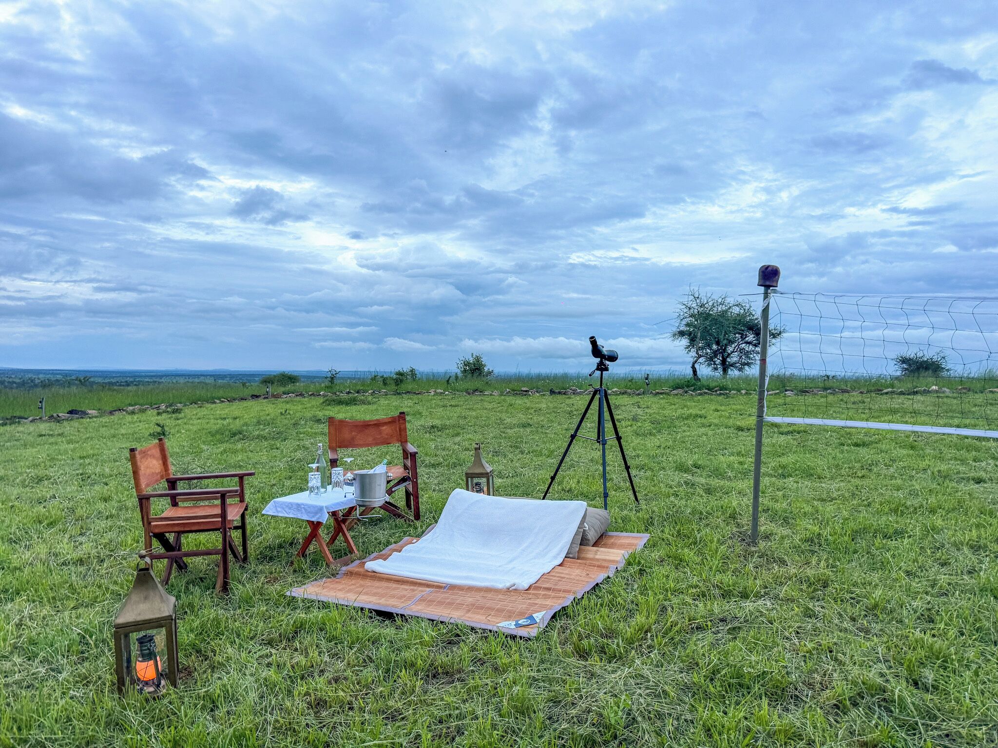 An outdoor picnic setup with a telescope, chairs, and a lantern on a grassy field.