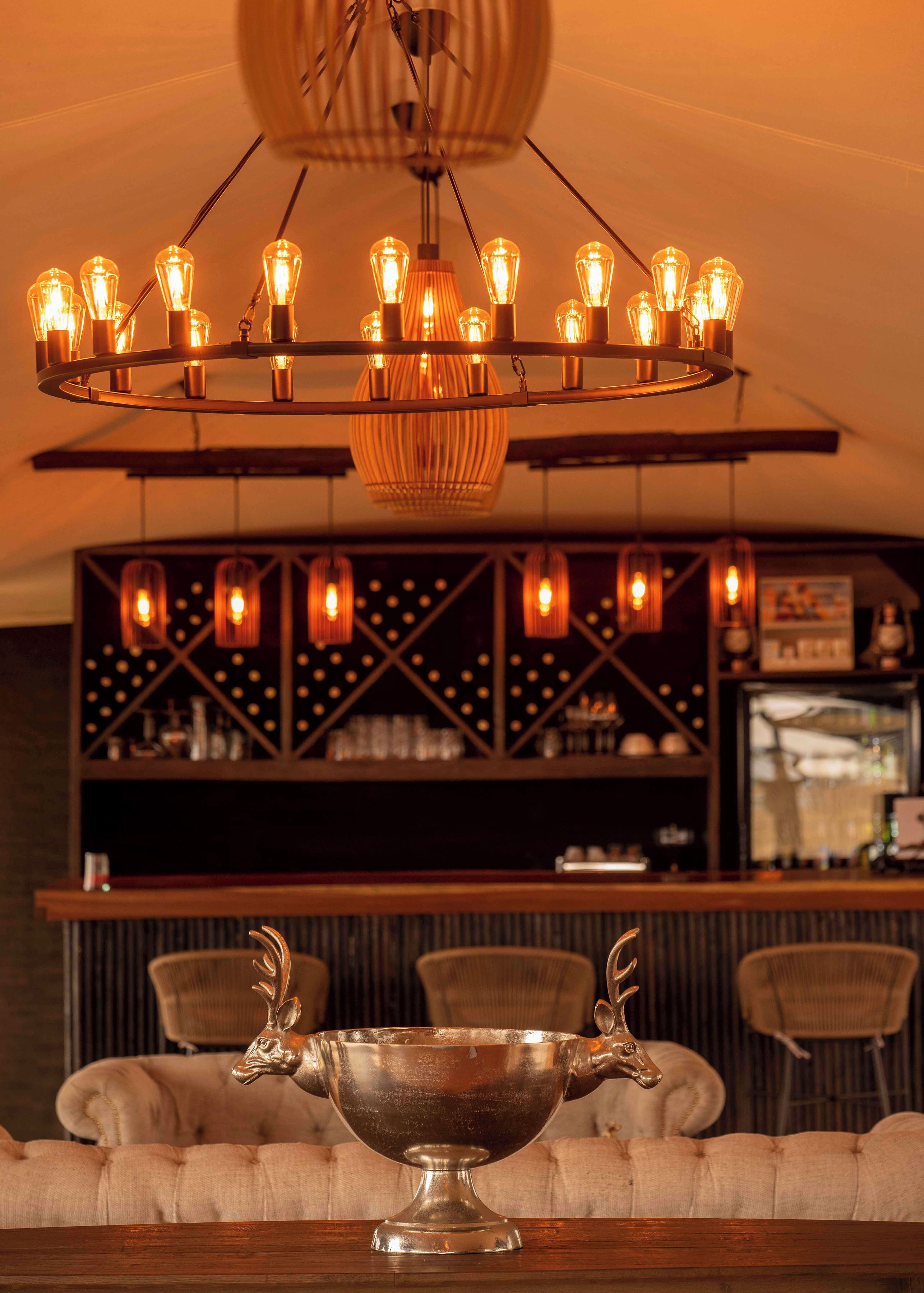 A bar area with a chandelier, cushioned seating, and a decorative silver bowl.