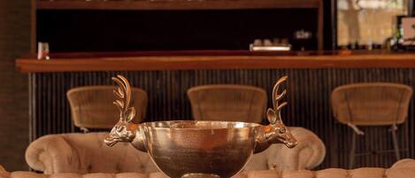 A bar area with a chandelier, cushioned seating, and a decorative silver bowl.