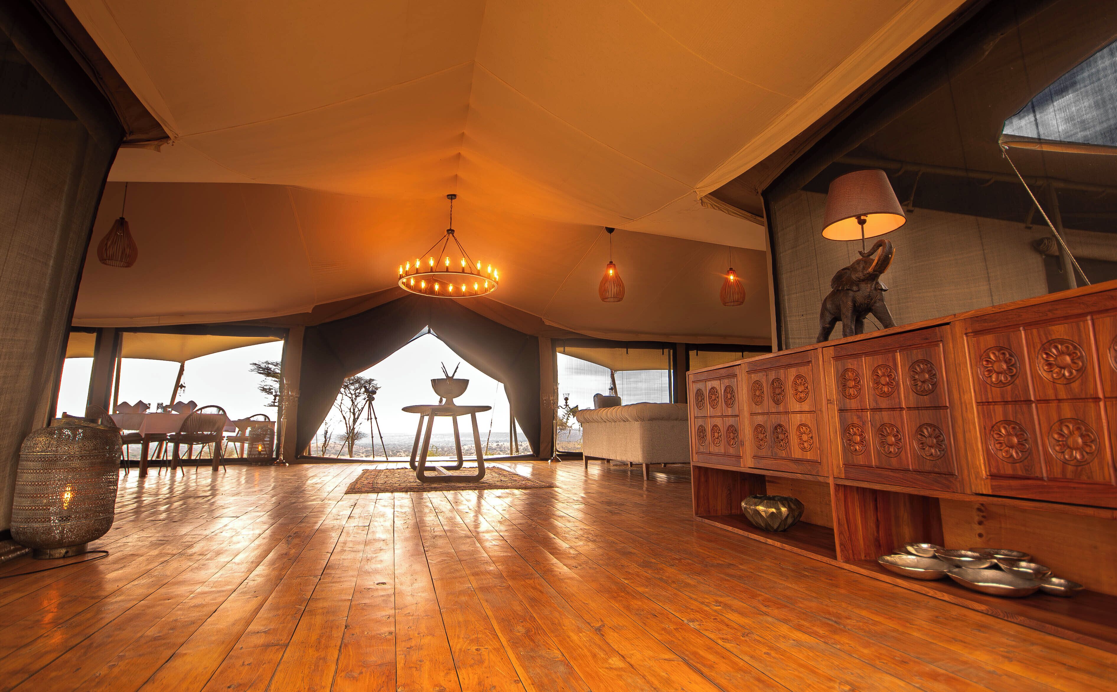 A spacious room with wooden floors, a chandelier, and a large window offering a view of the outdoors.