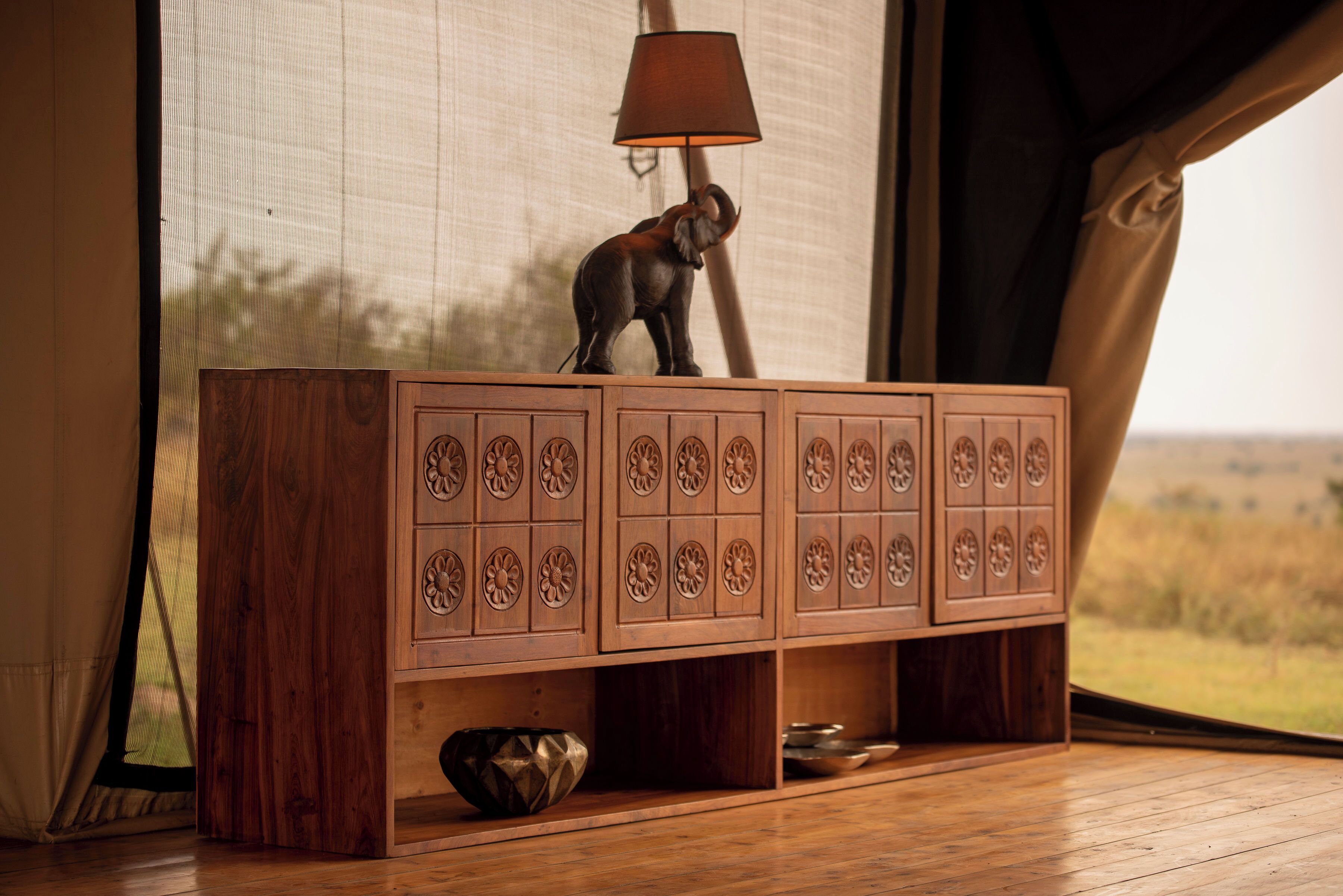 A wooden cabinet with intricate carvings, a lamp, and a view of a grassy field through a window.