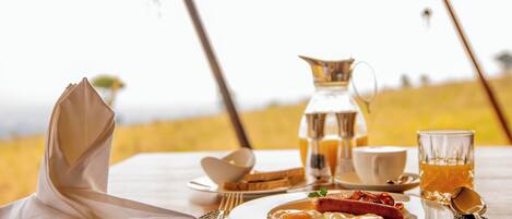 Un desayuno con un plato de comida, una jarra, una taza y un vaso de jugo sobre una mesa.